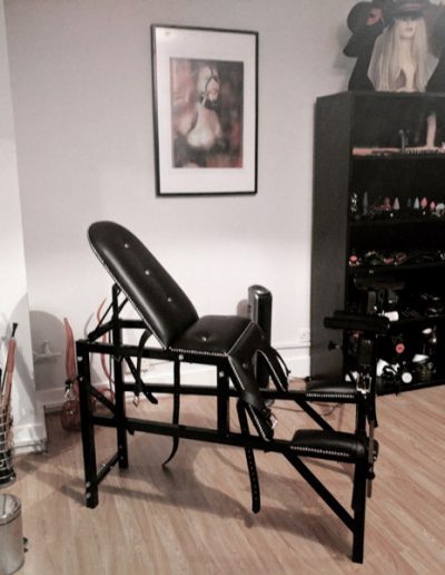 Room with specialized black reclining chair, art on walls, and shelves displaying various equipment.