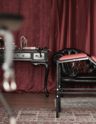 Vintage-style room with red decor, featuring a unique chair and leather sofa against a backdrop of elegant drapery.