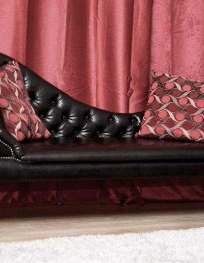 Elegant black leather tufted sofa with red patterned pillows, set against a luxurious red curtain backdrop.