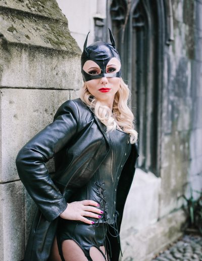 Woman in a leather cat costume posing against a stone wall, exuding confidence and mystery.