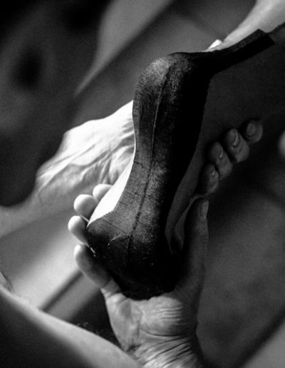 Black and white image of a person helping another put on a high heel shoe, showcasing elegance and care.