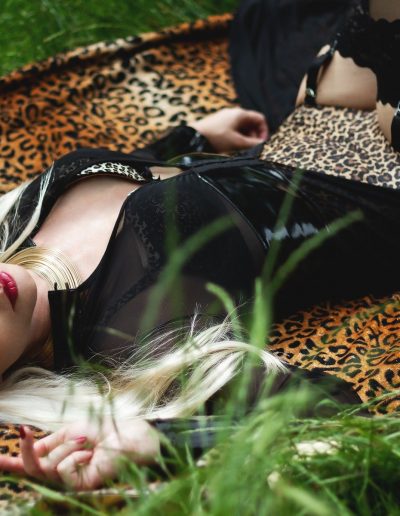 Blonde woman in sunglasses lying on a leopard print blanket outdoors, wearing black and leopard-print attire.