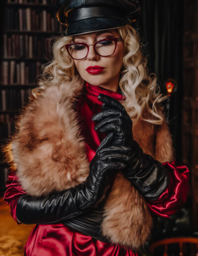Person in vintage style with fur scarf and leather gloves, wearing glasses and a leather hat, standing thoughtfully.